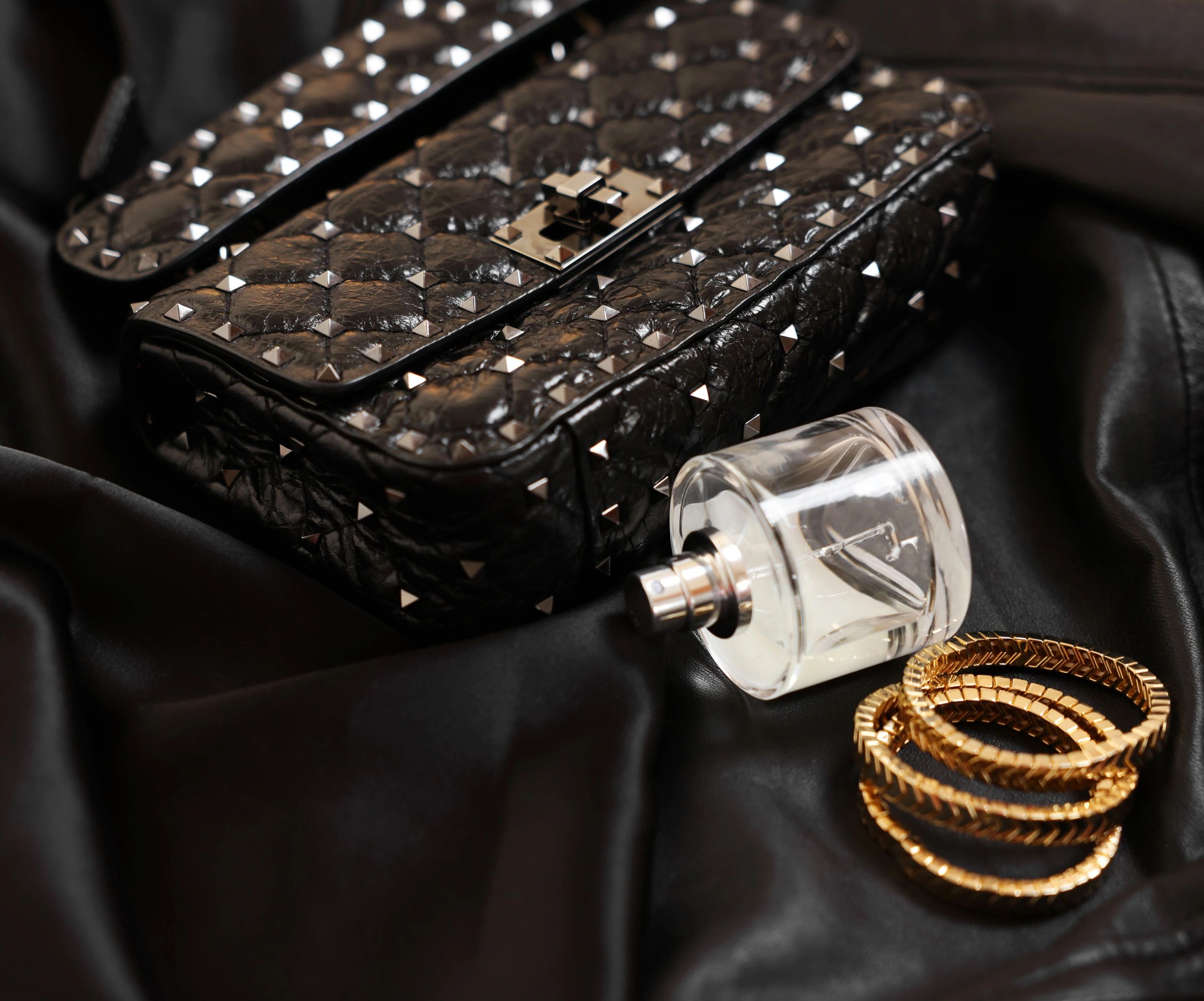 Leather bag, perfume and gold bracelets on black fabric